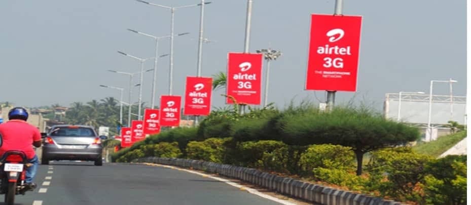 A run of red Airtel 3G median poles along a landscaped central reservation.