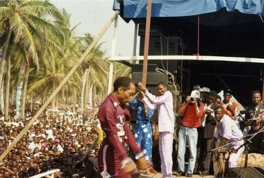 A performer on the Lekki Sunsplash stage at Maiyegun Beach, palm trees and a crowd stretching along the sand behind him.